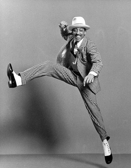 Vibrant dancing man in patterned suit and cowboy hat performing energetic dance move.