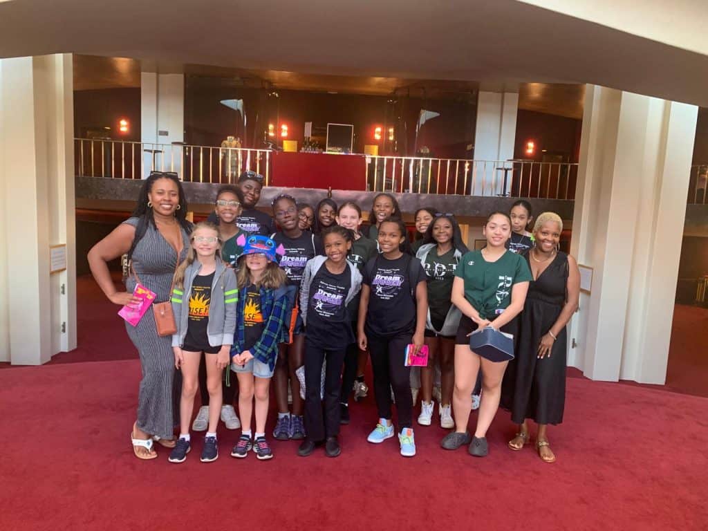 Diverse group of young girls and women at AbunDance event in a colorful, lively indoor venue.