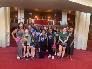 Diverse group of young girls and women at AbunDance event in a colorful, lively indoor venue.